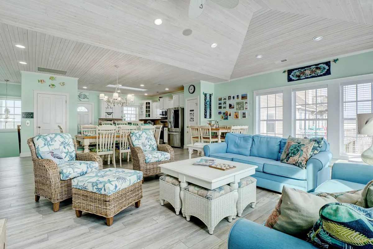 A cozy setting with a light blue sofa, woven armchairs, and a white coffee table, with a dining area visible in the background. This layout encourages both intimate conversation and larger social gatherings in a light-filled, relaxed space.