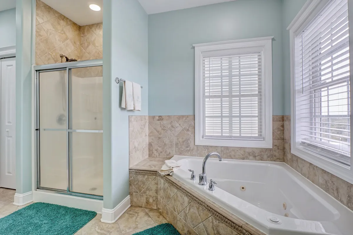 A spacious, serene bathroom with a bathtub and separate shower area, illuminated by natural light filtering through a window. The clean lines and tranquil ambiance evoke a sense of luxury and relaxation.
