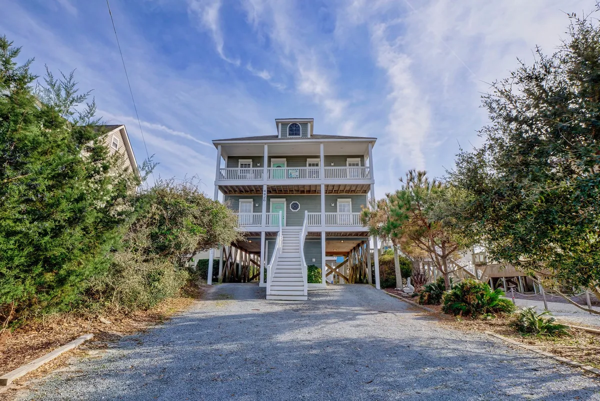 An exterior shot of the house with stairs leading up to the entrance and lush greenery surrounding the property. The structure hints at the elevations that provide sweeping views from various decks, capturing both the home’s inviting presence and its integration with natural surroundings.