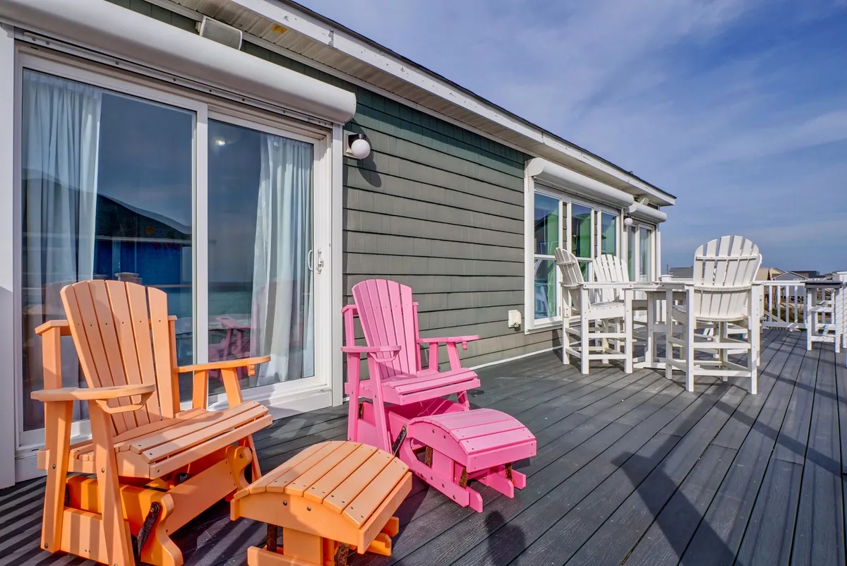 A cheerful wooden deck featuring colorful Adirondack chairs and sliding glass doors, with open views ideal for relaxing outdoors. The scene evokes a sense of leisure and social gathering, inviting guests to enjoy the scenery and fresh air.