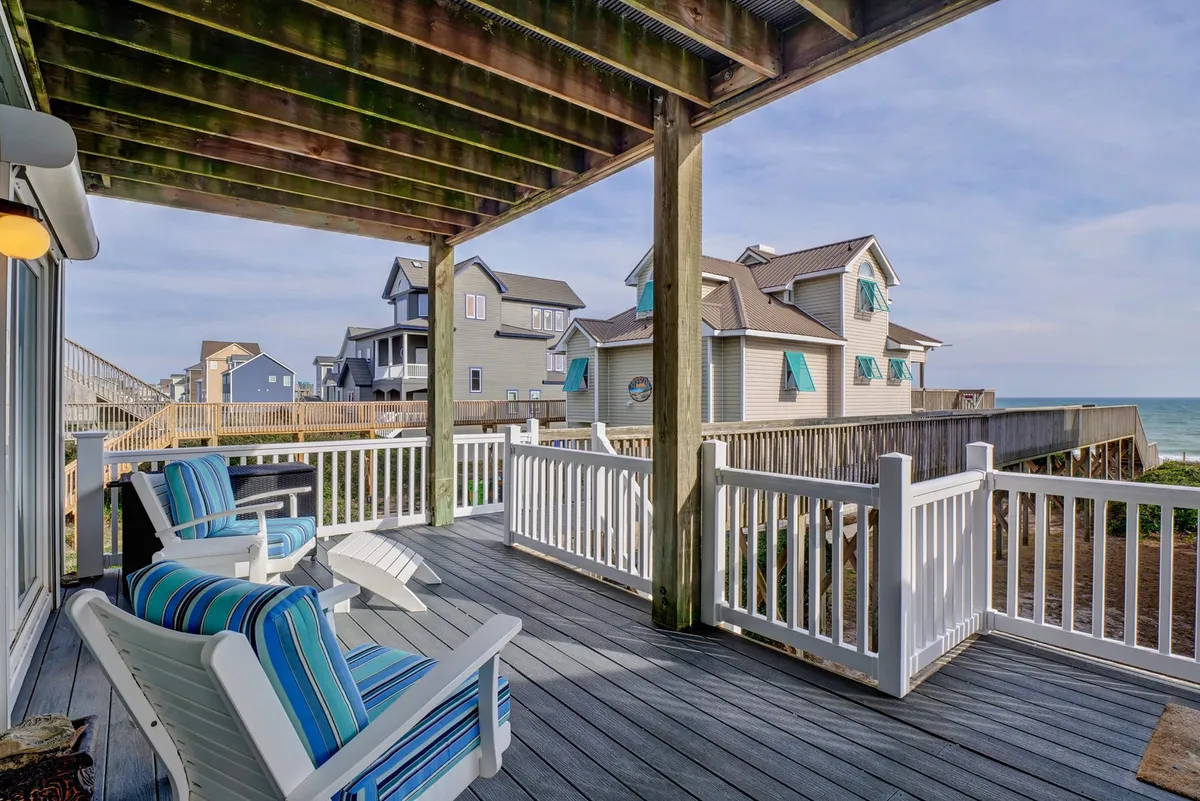 A tranquil exterior scene featuring deck chairs lined along a wooden deck, framed by a railing with an uninterrupted ocean view beyond. The early morning light or soft evening glow suggests moments of relaxation and quiet contemplation, with the inviting blue expanse of the sea as a backdrop.