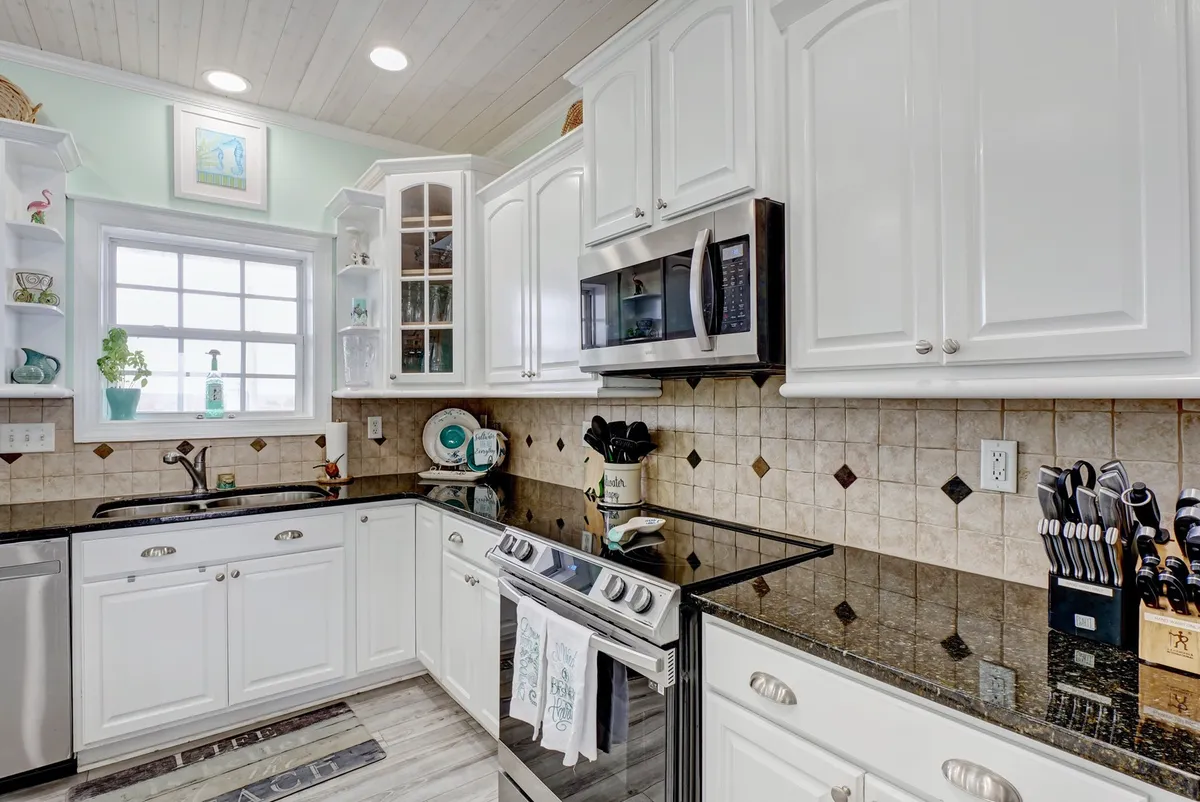 A vibrant and welcoming kitchen featuring white cabinetry, granite countertops, modern appliances, and a window that fills the space with natural light. Decorative items on the shelves add a touch of personality, while the open layout supports effortless movement and conversation during meal preparation.